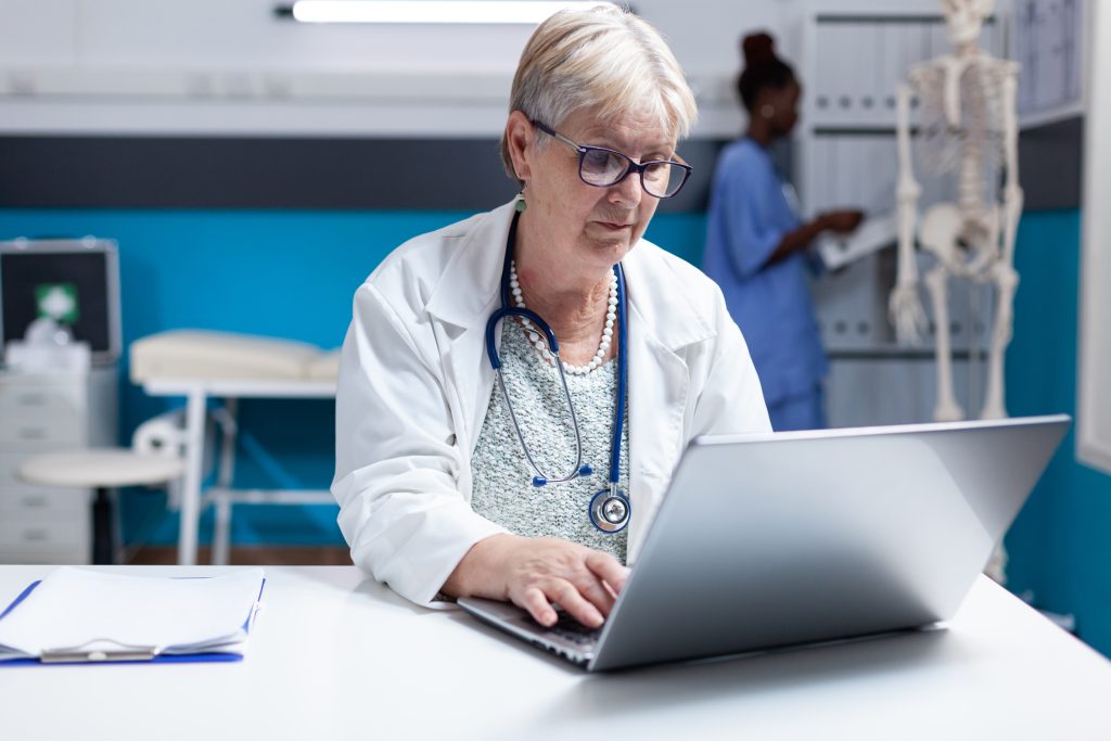 Portrait of medic with stethoscope using laptop to work on healthcare in cabinet