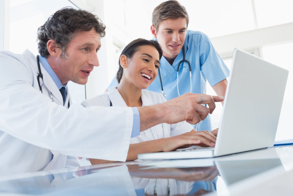Team of happy doctors working on laptop computer in medical office