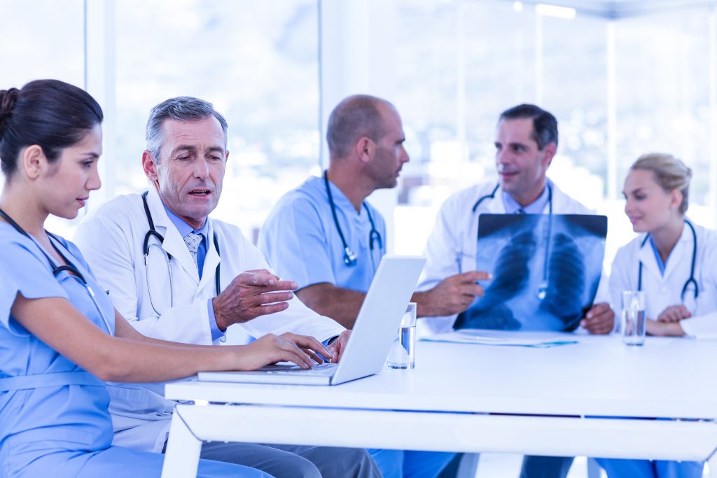 Doctors using computer whiles theirs colleagues looking at Xray in medical office